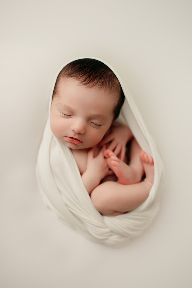 Newborn Photography, baby swaddled up in white blanket with feet tucked in